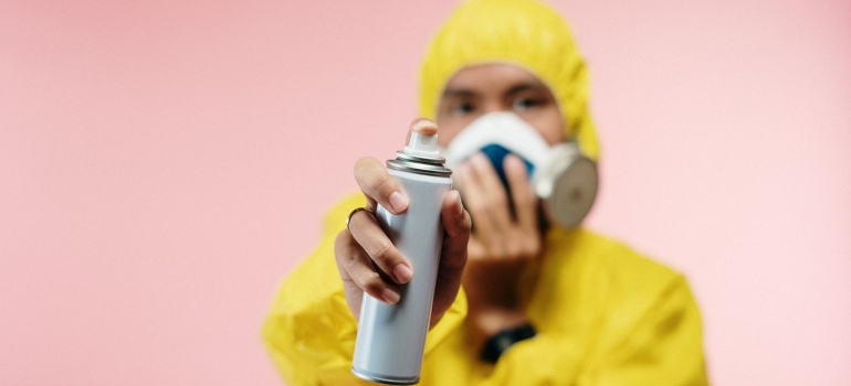 A person in a jumpsuit using spray to prevent birds from nesting.