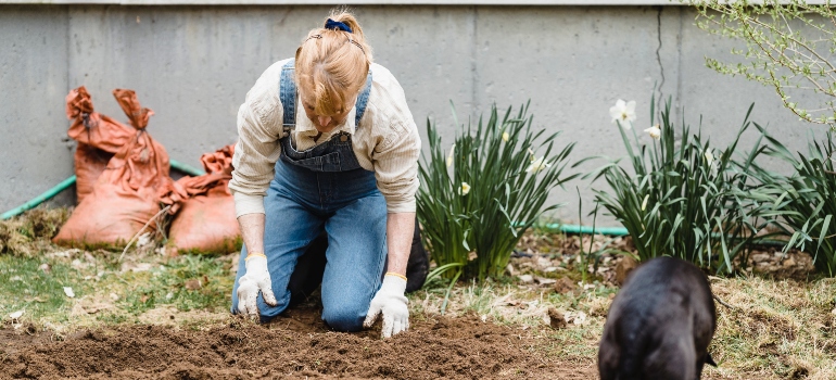a woman kneeling in the garden to prepare soil for turfing