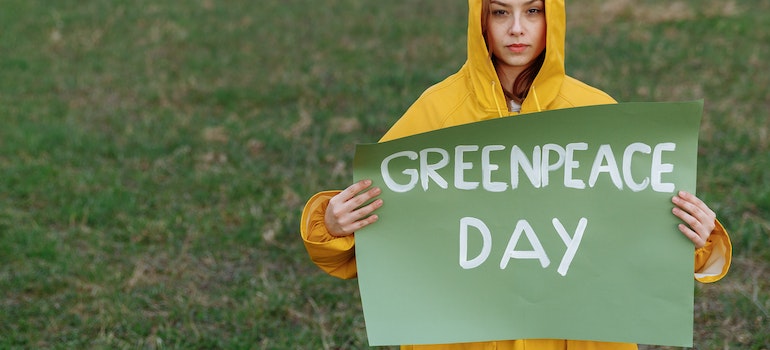 A woman on artificial grass holding greenpeace day sign